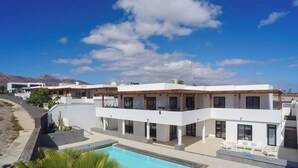 Una casa moderna de dos pisos con piscina, ventanas amplias y una vista despejada de las montañas.
