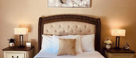A neatly made bed with a tufted headboard, flanked by two bedside tables with lamps and a vase of flowers.