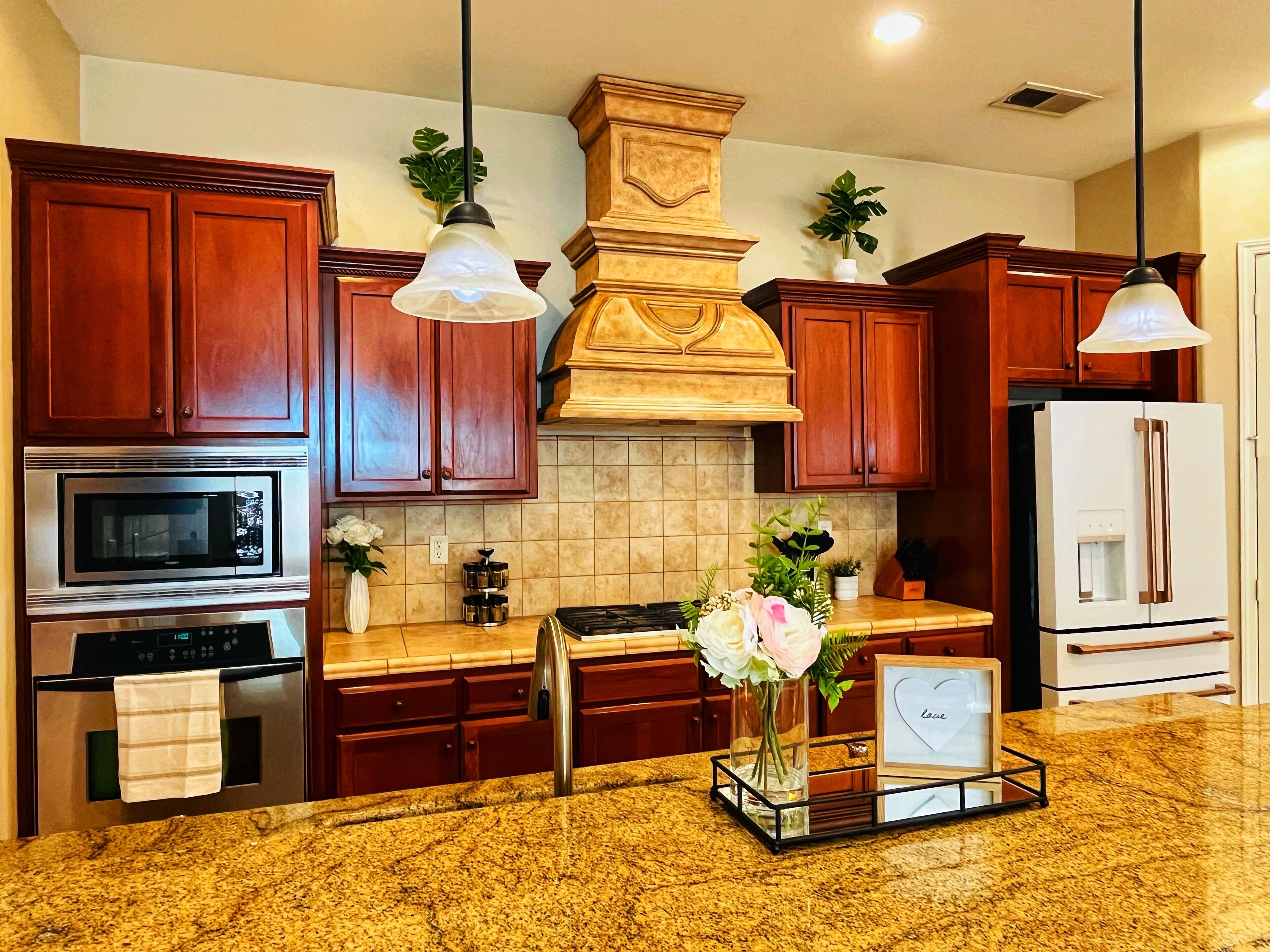 Una cocina con armarios de madera, electrodomésticos de acero inoxidable, encimeras de granito e iluminación colgante.