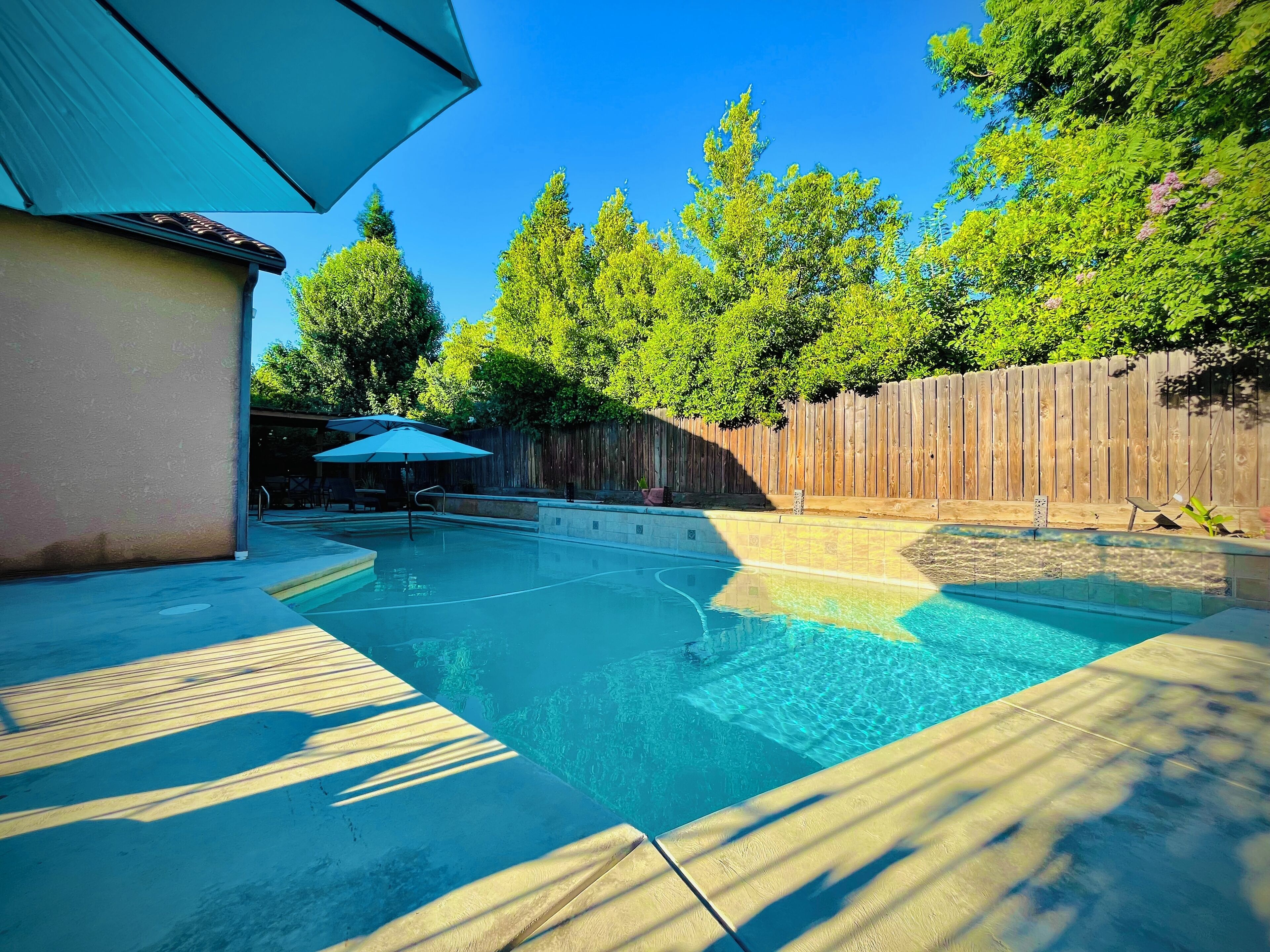 A backyard with a swimming pool, a wooden fence, and a patio area with an umbrella.