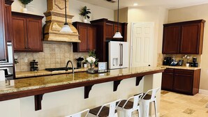 Una cocina con armarios de madera oscura, encimera de granito, refrigerador blanco y una barra con taburetes blancos.