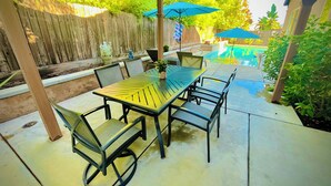 Un patio al aire libre con una mesa y sillas, rodeado por una valla de madera y una piscina.