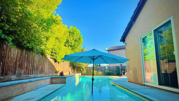 Una piscina con una sombrilla azul, rodeada por una valla de madera y una casa.