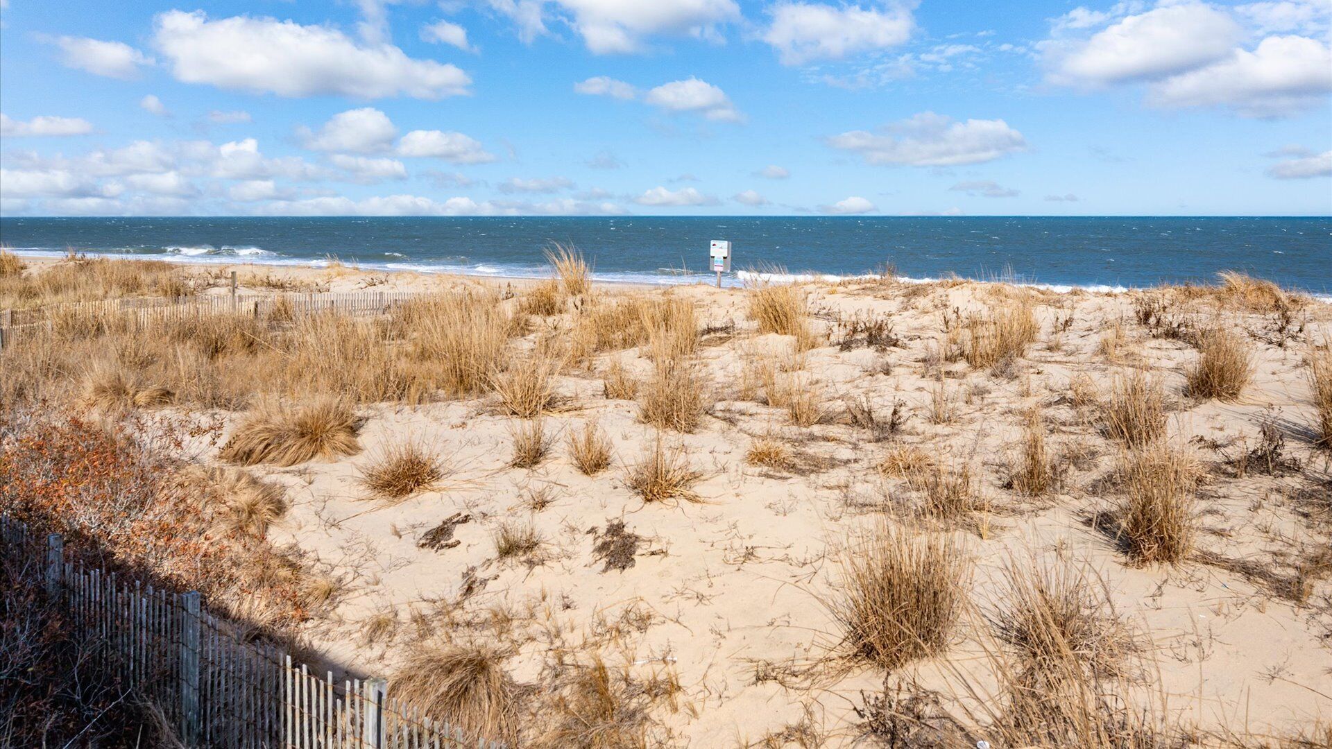 A beach with dunes, a wooden fence, and a lifeguard tower.