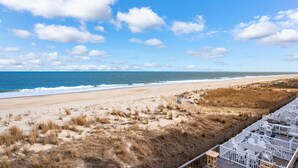 A beach view with a wooden fence, a sandy beach, and a white building with outdoor seating. - Oceanfront Private Home With Amazing Views (Ocean City)