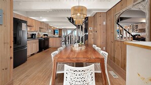 A wooden interior with a dining table, chairs, a chandelier, and a kitchen area with appliances. - Oceanfront Private Home With Amazing Views (Ocean City)