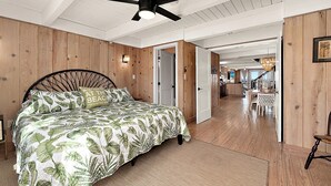 A bedroom with a bed, a ceiling fan, wooden walls, and a view into the kitchen. - Oceanfront Private Home With Amazing Views (Ocean City)