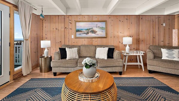 A room with a wooden paneled wall, two sofas, a round coffee table with a vase, and a painting above the sofas. - Oceanfront Private Home With Amazing Views (Ocean City)