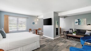 Quarto de hotel moderno com uma cama grande, um sofá, uma mesa de centro e uma TV na parede.