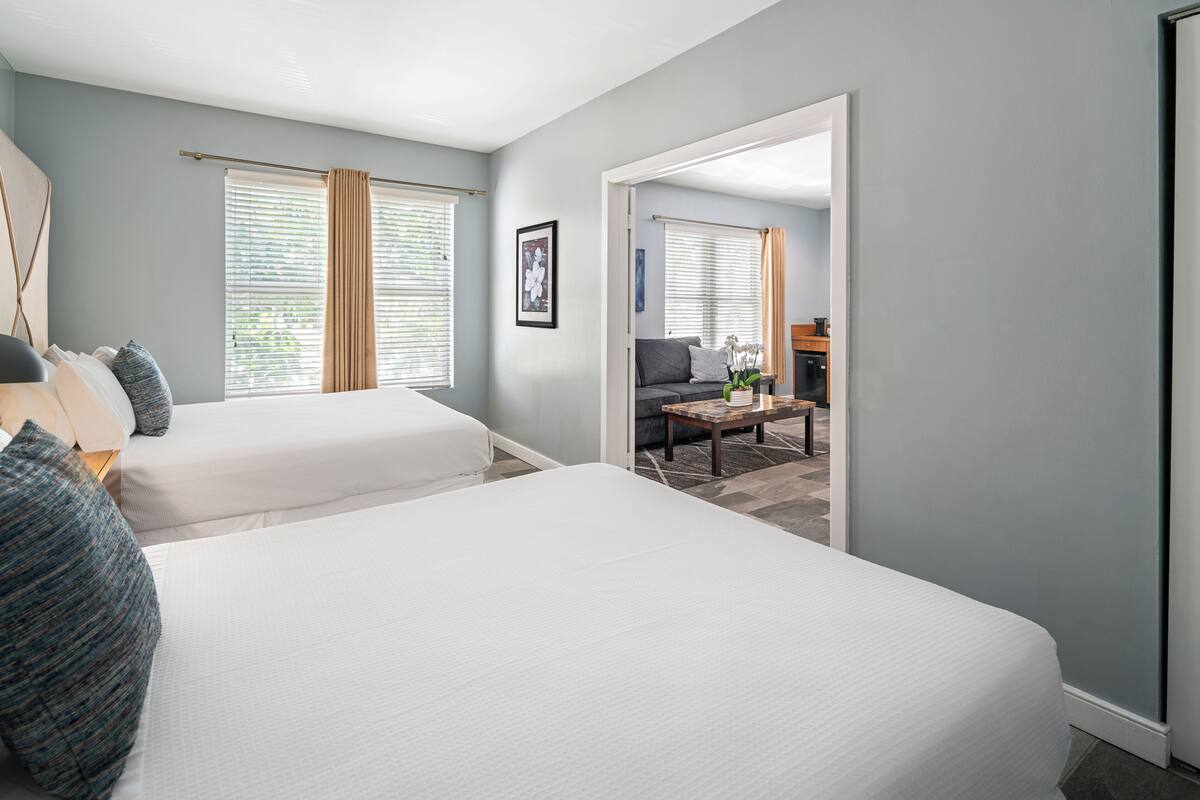 A hotel room with two beds, a sofa, a coffee table, and a view of the dining area.
