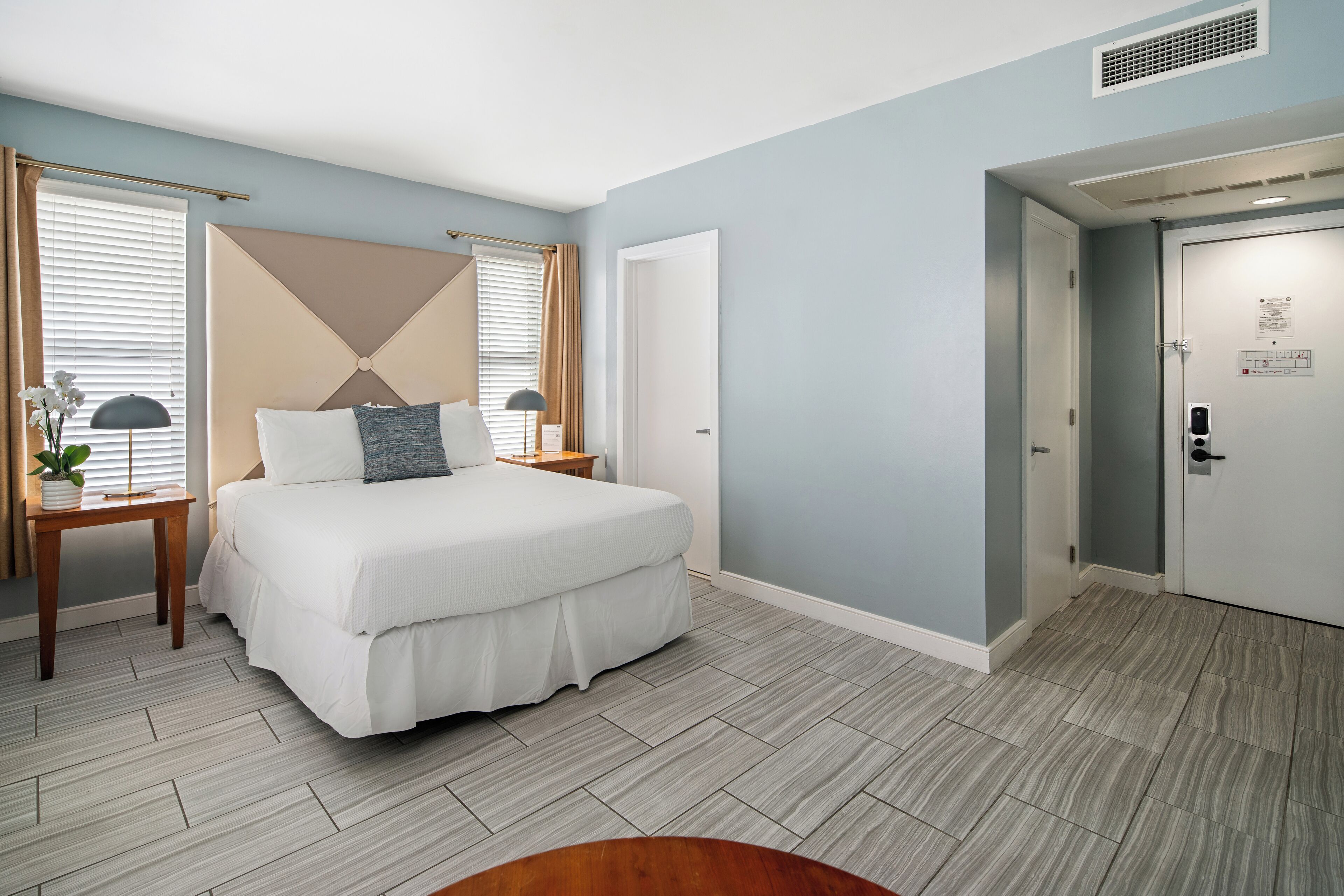 Une chambre à coucher avec un grand lit, une table de chevet, une commode, une fenêtre avec des rideaux et une porte avec une serrure.