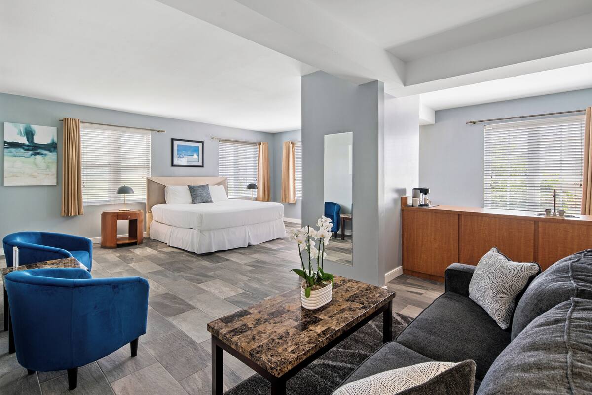 A modern hotel room with a bed, a sofa, a coffee table, and a desk area.