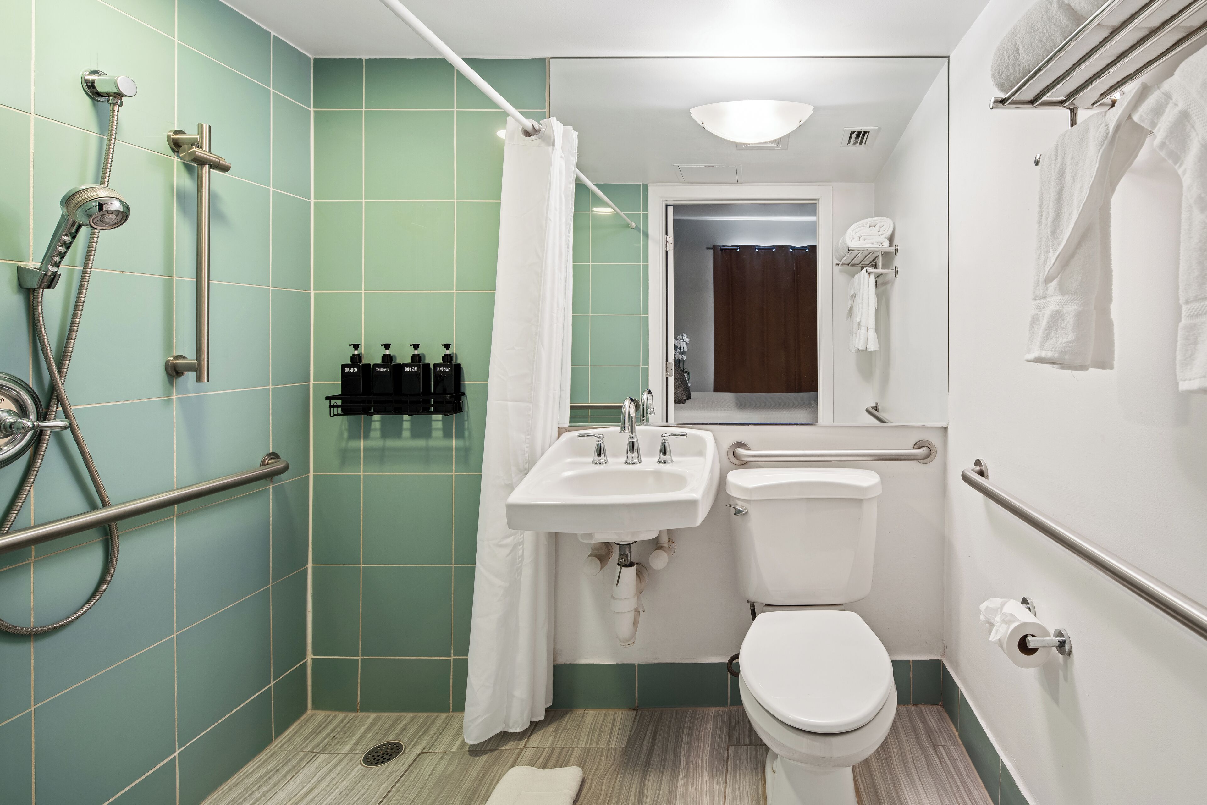 A bathroom with a shower, toilet, sink, and handrails.