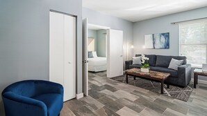 Uma sala de estar moderna com uma poltrona azul, um sofá cinzento e uma mesa de centro com uma planta.