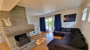 Ein geräumiges Wohnzimmer mit Kamin aus Stein, einer dunkelbraunen Sofagarnitur und einem großen Fenster mit Vorhängen.