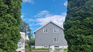 Ein zweistöckiges Haus mit grauer Fassade, einer Flagge und einem Garten mit Gartenmöbeln.