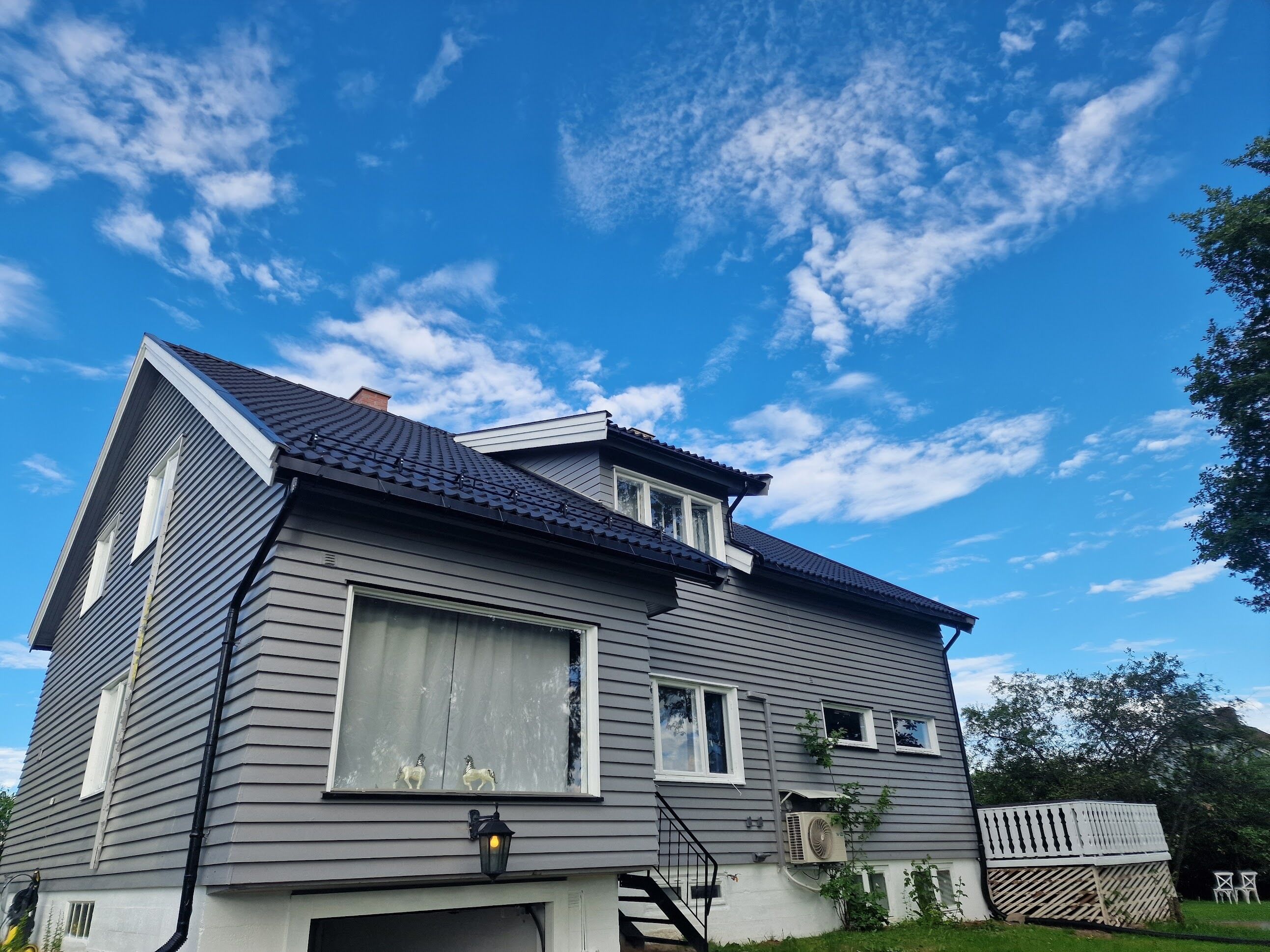Ein zweistöckiges Haus mit dunklem Dach, Garage und kleiner Veranda.