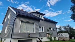 Ein zweistöckiges Haus mit dunklem Dach, Garage und kleiner Veranda.
