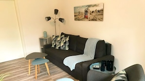 Una sala de estar moderna con un sofá oscuro, dos mesitas y un cuadro en la pared.