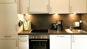 Cocina moderna con armarios blancos, encimera negra, estufa, horno, cafetera y fregadero.