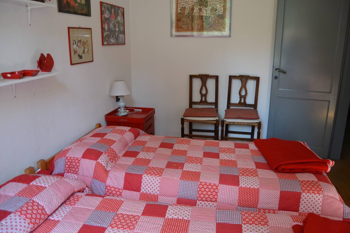 Ein Schlafzimmer mit einem Bett, zwei Stühlen, einem Nachttisch, einer Lampe und einer Tür.