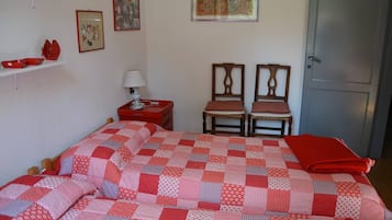 A bedroom with a bed, two chairs, a nightstand, a lamp, and a door.