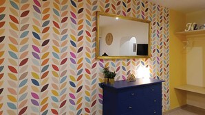 A room with a patterned wallpaper, a blue dresser, a mirror, and a shelf with a TV. - Vacation home in the center 5 minutes from the National Museum, Duomo, Sanita (Napoli)