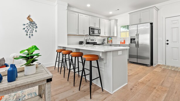 Cocina moderna con armarios blancos, un refrigerador de acero inoxidable y una isla central con taburetes de bar.