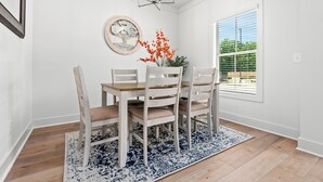 Un comedor con una mesa y sillas de madera, una araña, un cuadro enmarcado y una ventana con persianas.
