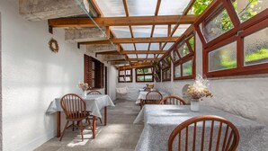 A rustic dining area with wooden tables and chairs, a stone floor, and large windows with wooden frames. - Lovely apartment in Divaca with WiFi (Divaca)