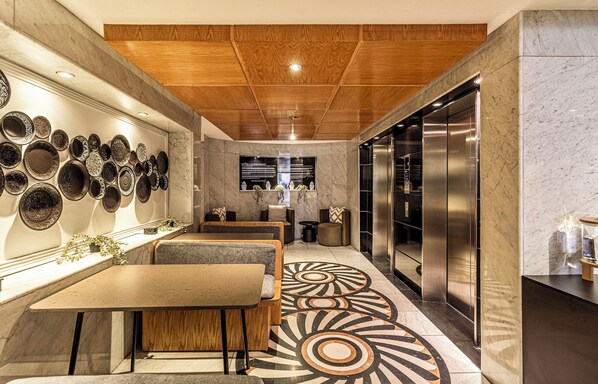 A modern interior with a wooden ceiling, a wall of decorative plates, a seating area, and a large elevator.