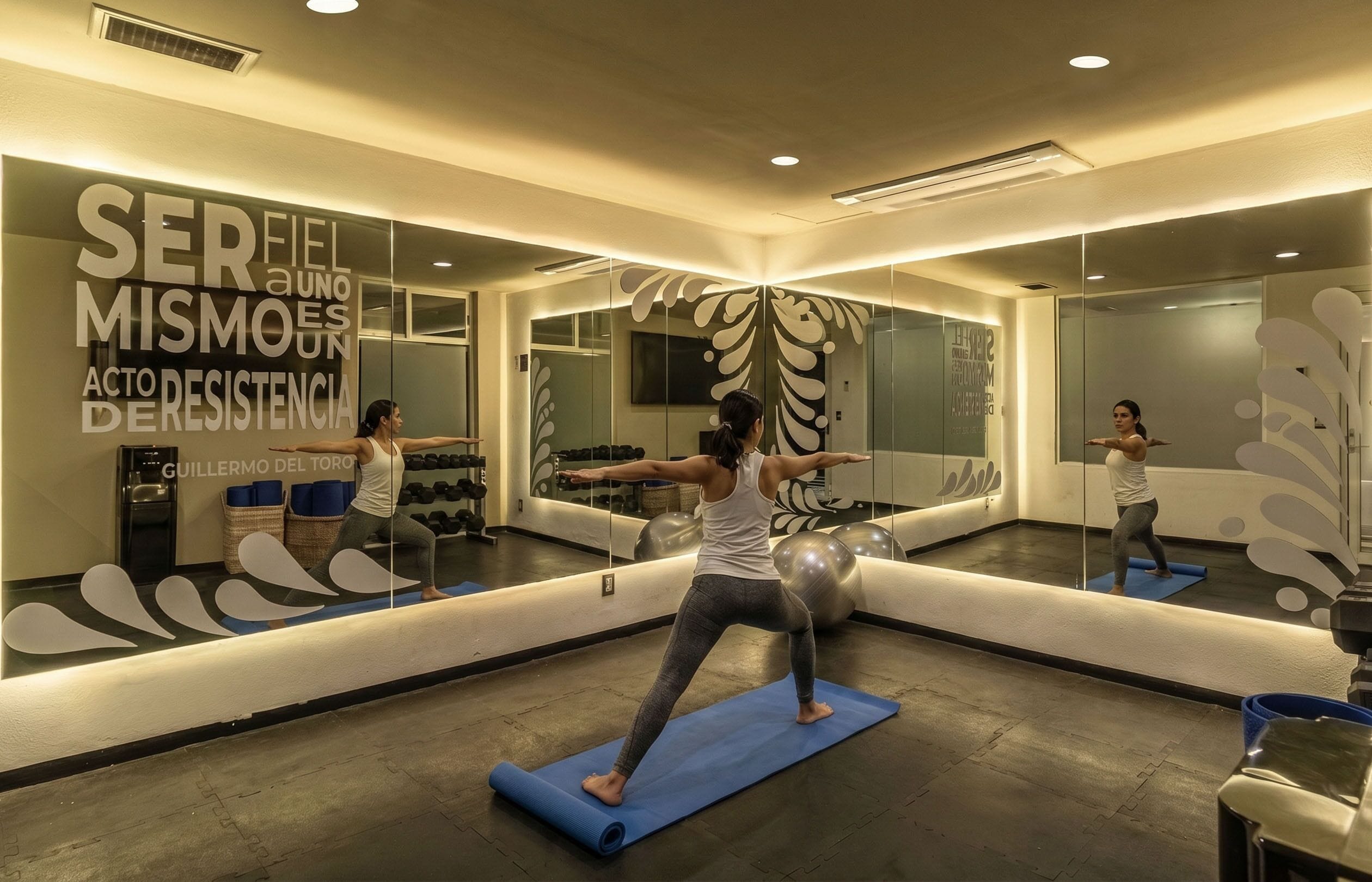 Un gimnasio con paredes espejadas, equipo de ejercicio y una frase motivacional.