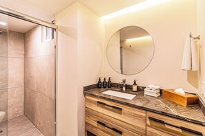 A modern bathroom with a glass shower enclosure, a marble countertop, wooden vanity, and a round mirror. - Kukun Grand Chapultepec (Mexico City)
