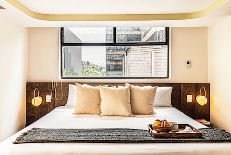 A hotel room with a large bed, a window with a city view, and a tray with fruits on the bed.. Kukun Grand Chapultepec