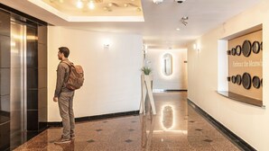 A modern hotel lobby with a polished floor, a large mirror with plates, and an elevator. - Kukun Grand Chapultepec (Mexico City)