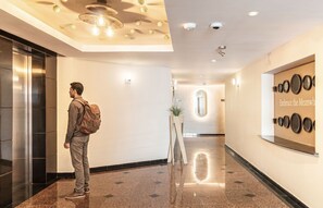 Eine moderne Hotelhalle mit einem polierten Boden, einem großen Spiegel mit Tellern und einem Aufzug.