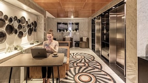 A modern interior with a wooden ceiling, a wall of decorative plates, a seating area with a laptop, and a large elevator. - Kukun Grand Chapultepec (Mexico City)