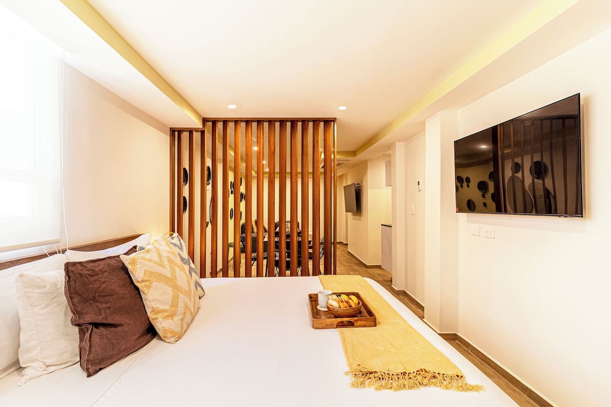 Habitación de hotel con cama, almohadas, bandeja con comida, televisor y un separador de madera.