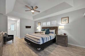 A bedroom with a bed, nightstands, a ceiling fan, and a door leading to another room.