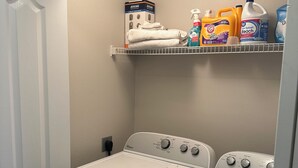 Ein Waschraum mit zwei Whirlpool-Waschmaschinen, einem Regal mit Reinigungsmitteln und einer Tür.