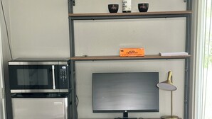 Eine kompakte Küchenzeile mit Mikrowelle, Kühlschrank und einem kleinen Computertisch mit Bildschirm, Tastatur und Lampe.