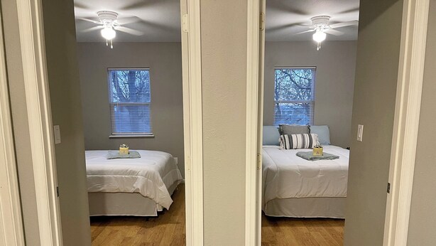 Ein Spiegelbild zeigt ein Schlafzimmer mit zwei Betten, Holzboden, Deckenventilatoren und Fenstern mit Jalousien.
