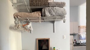 A neatly organized room with a white console table, a mirror, and a framed picture. There are shelves with folded towels and baskets, and a small kitchen area in the background. - Cozy studio in enchanting New Orleans Neighborhood with AC, WiFi (New Orleans)