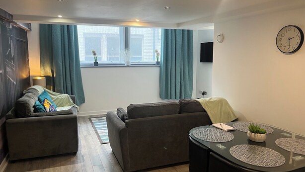 A modern living room with two sofas, a dining table with placemats, a clock, and a window with curtains. - Location, Location, city centre apartment, 2 bedrooms, 2 bathrooms (Liverpool)