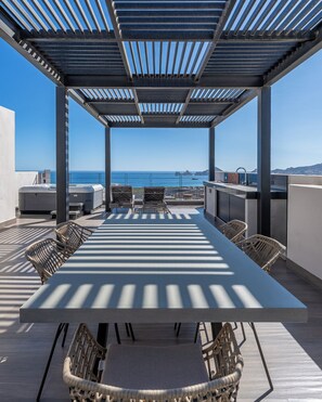 Une terrasse sur le toit, avec une longue table et des chaises en osier, d’où l’on a une vue sur l’océan.