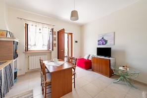 A compact living space with a dining table, chairs, a red sofa, a TV, and a glass table.