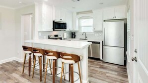 A modern kitchen with white cabinetry, a stainless steel refrigerator, a microwave, and a bar area with stools. - Fisherman Dream Waterfront Home with Private Dock (Surfside Beach)