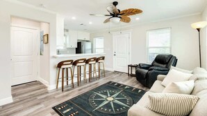 A modern living room with a ceiling fan, a bar area with stools, a leather sofa, and a compass-themed rug. - Fisherman Dream Waterfront Home with Private Dock (Surfside Beach)