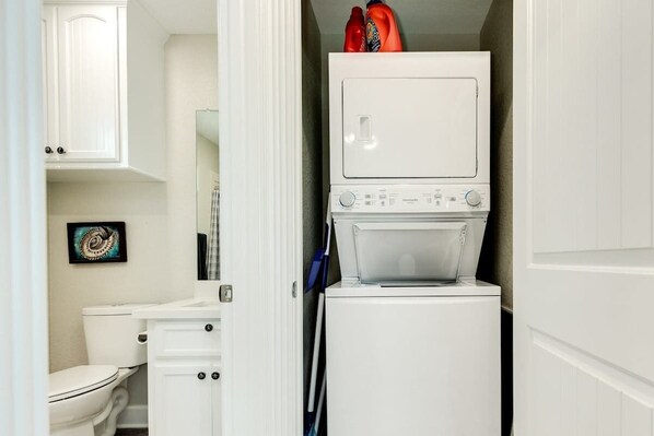 Une petite buanderie avec des appareils superposés, des toilettes et un meuble de rangement.