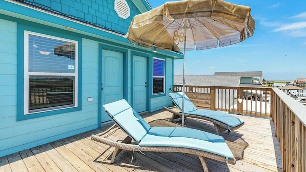 A turquoise building with a wooden deck, two lounge chairs, and a beach umbrella. - Fisherman Dream Waterfront Home with Private Dock (Surfside Beach)